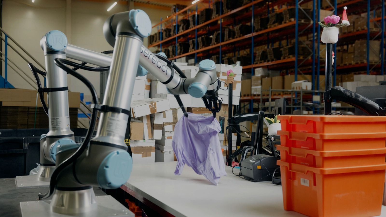 Photo officielle Universal Robots et Sereact : deux bras robotisés saisissent un vêtement retourné dans un entrepôt